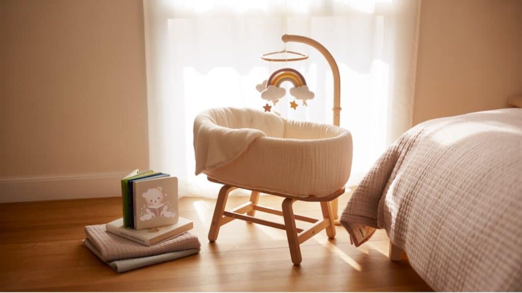Minimalist baby sleep setup with bassinet near bed and subtle rainbow mobile overhead